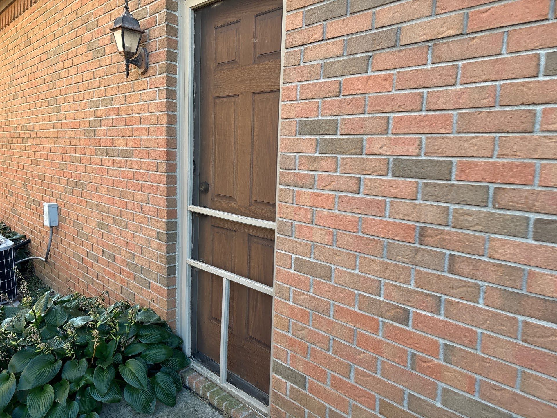 Brick House Front Door With Screen Lawton Residence exterior: brick wall, wooden door, and screen door.