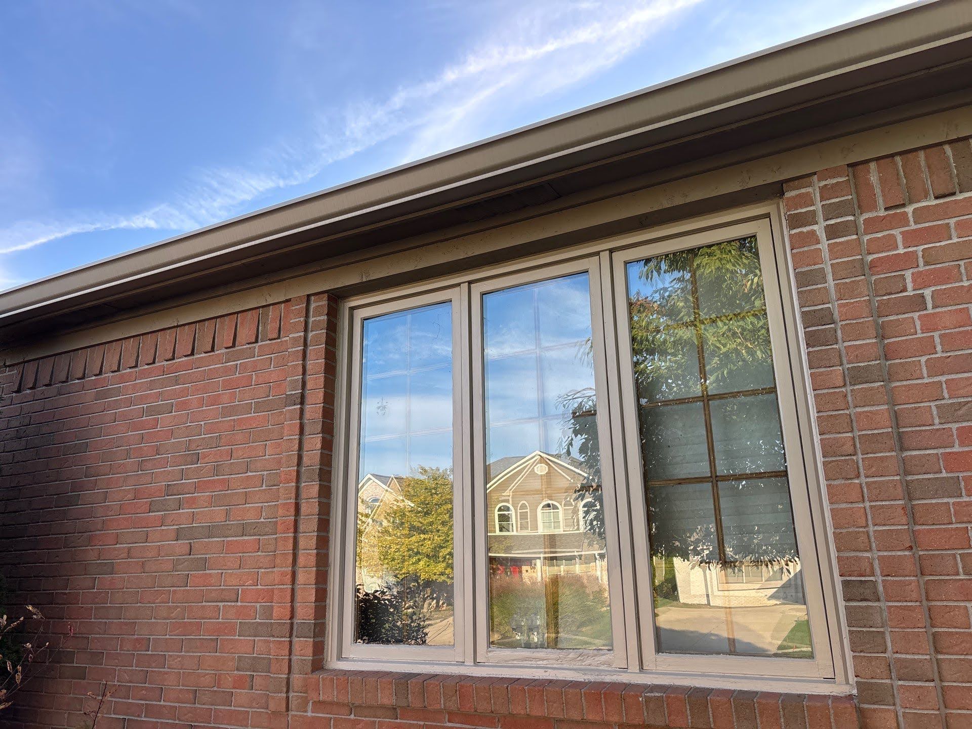 Brick House Reflection Window Daylight Lawton Residence exterior: brick wall with window reflecting houses and trees.