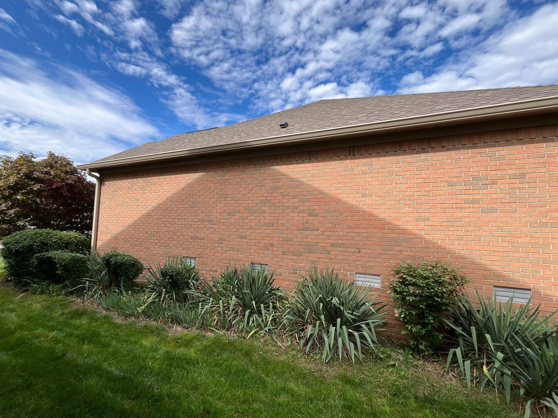 Brick House Side With Landscaping And Blue Sky Lawton Residence exterior: brick wall, green lawn, and blue sky with clouds.