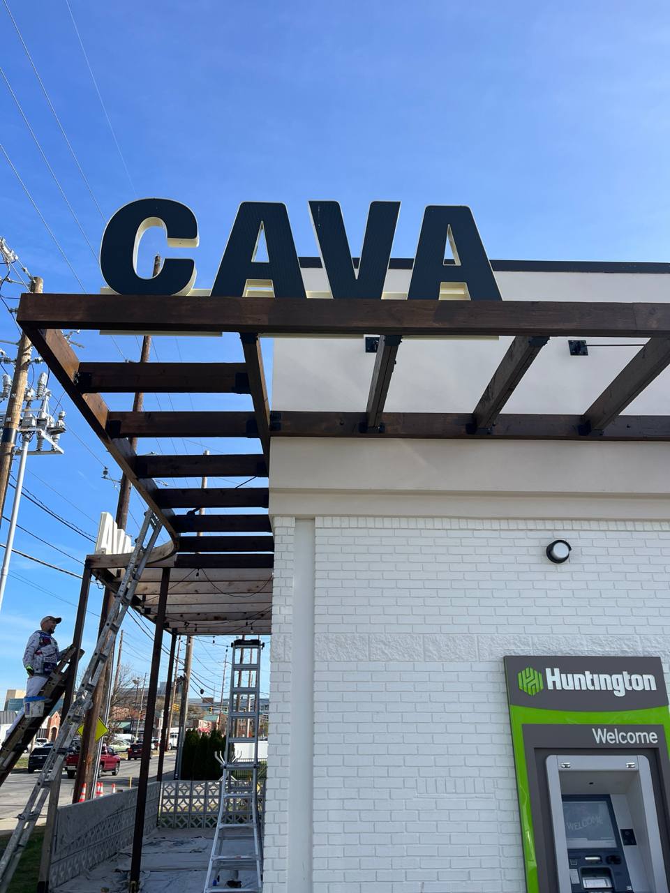 Cava Restaurant Exterior Sign Installation Cava canopy exterior staining: Painter on ladder near Cava restaurant sign.