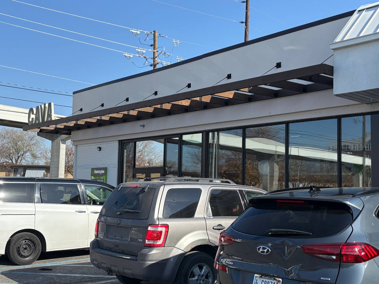 Cava Restaurant Exterior With Cars CAVA exterior with stained wooden canopy and parked cars.