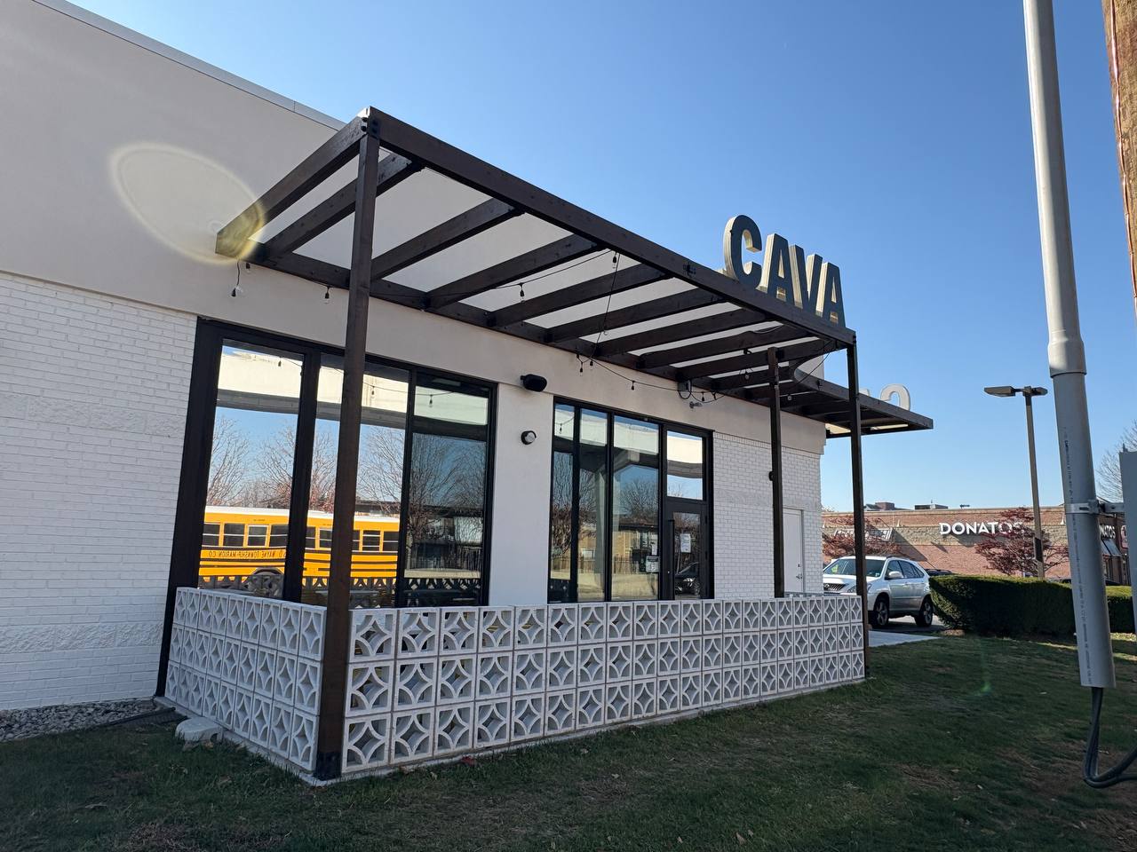 Cava Restaurant Exterior With Patio And School Bus Exterior of Cava restaurant with a dark wood canopy, white brick building, and decorative concrete wall.