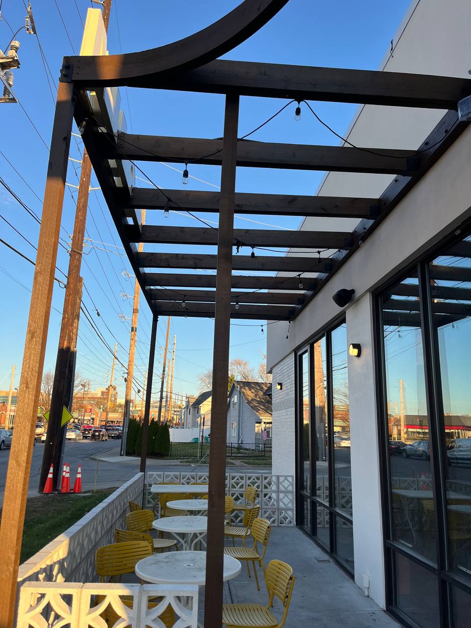 Outdoor Dining Area With Yellow Chairs And Tables Exterior view of Cava restaurant with stained wood pergola and outdoor seating