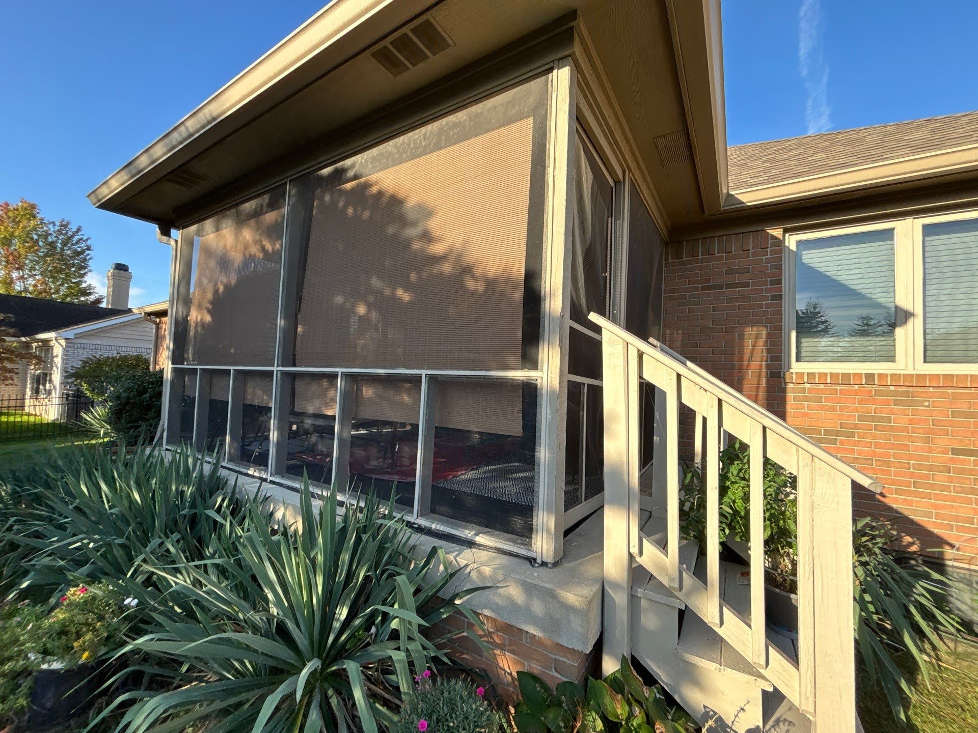 Screened Porch With Railing And Plants Screened-in porch with beige blinds and wooden railing, part of Lawton Residence exterior.