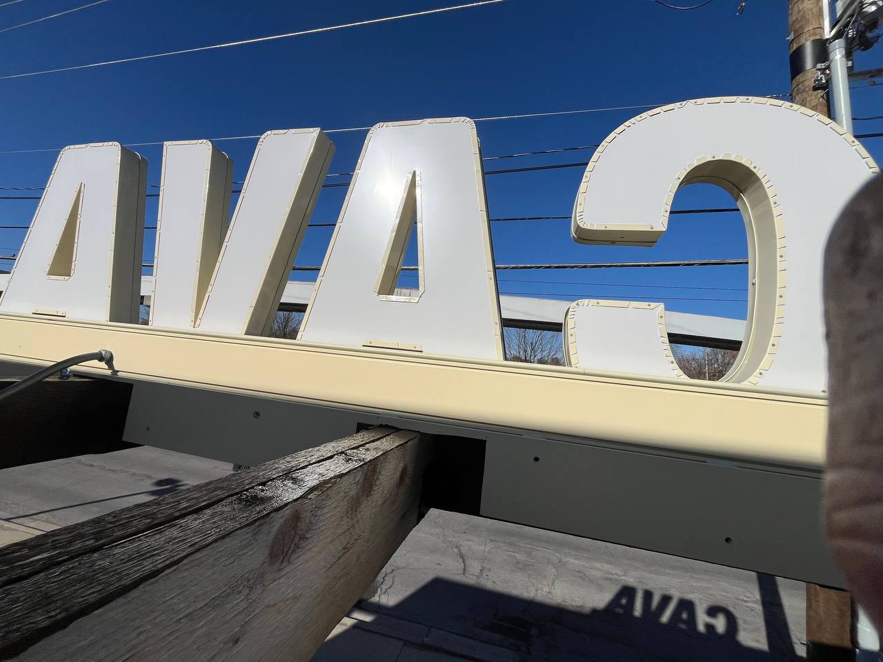 White Ava Sign On Wood Structure Cava canopy exterior staining: Large white "Cava" sign on a cream-colored canopy.