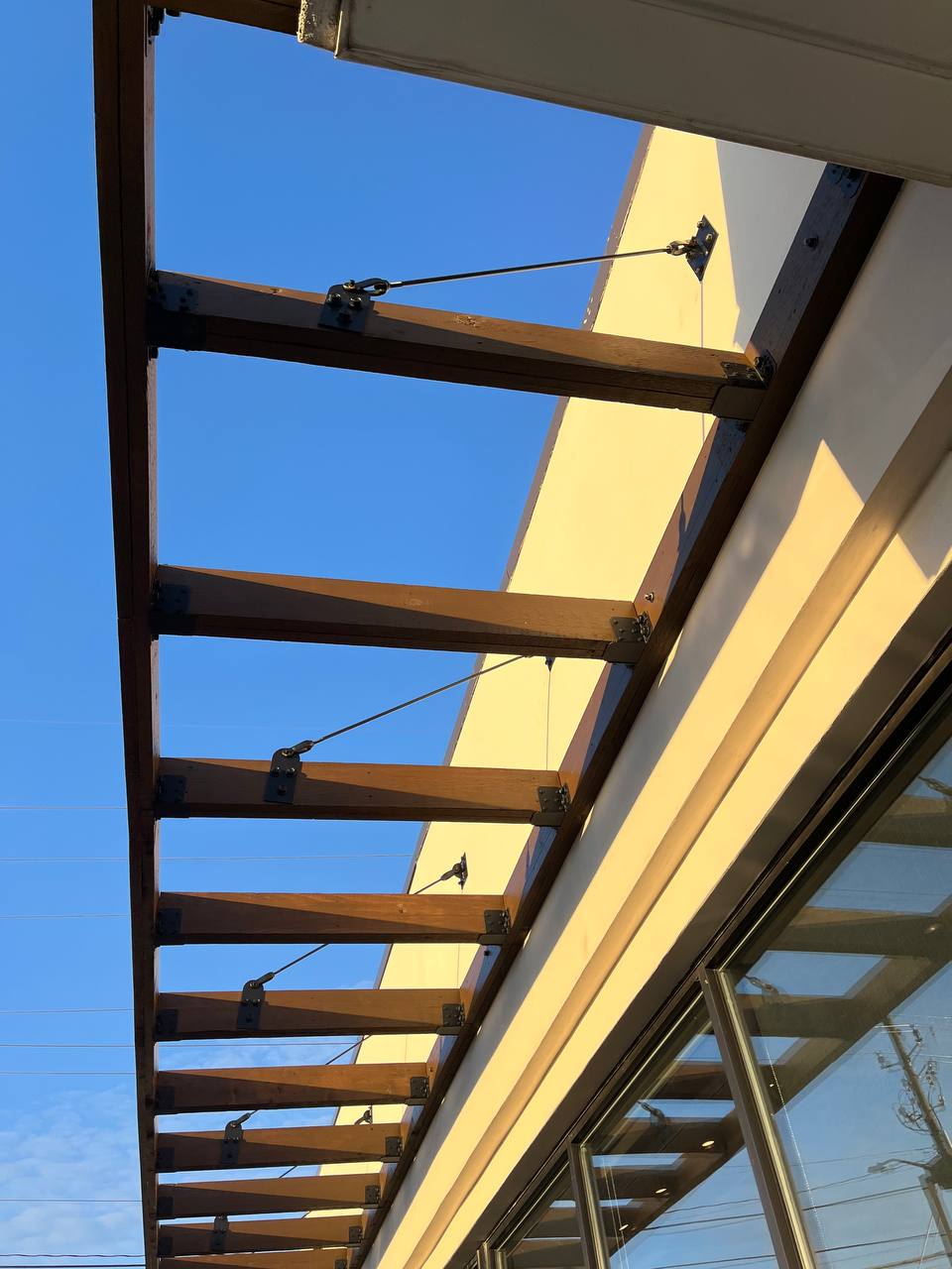 Wooden Pergola Support Structure With Cables Cava canopy exterior staining: stained wooden beams against blue sky.