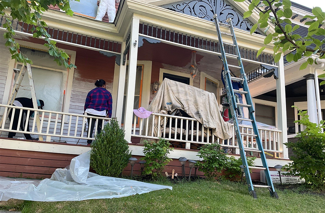 Professional painters scraping and preparing a home's exterior before painting