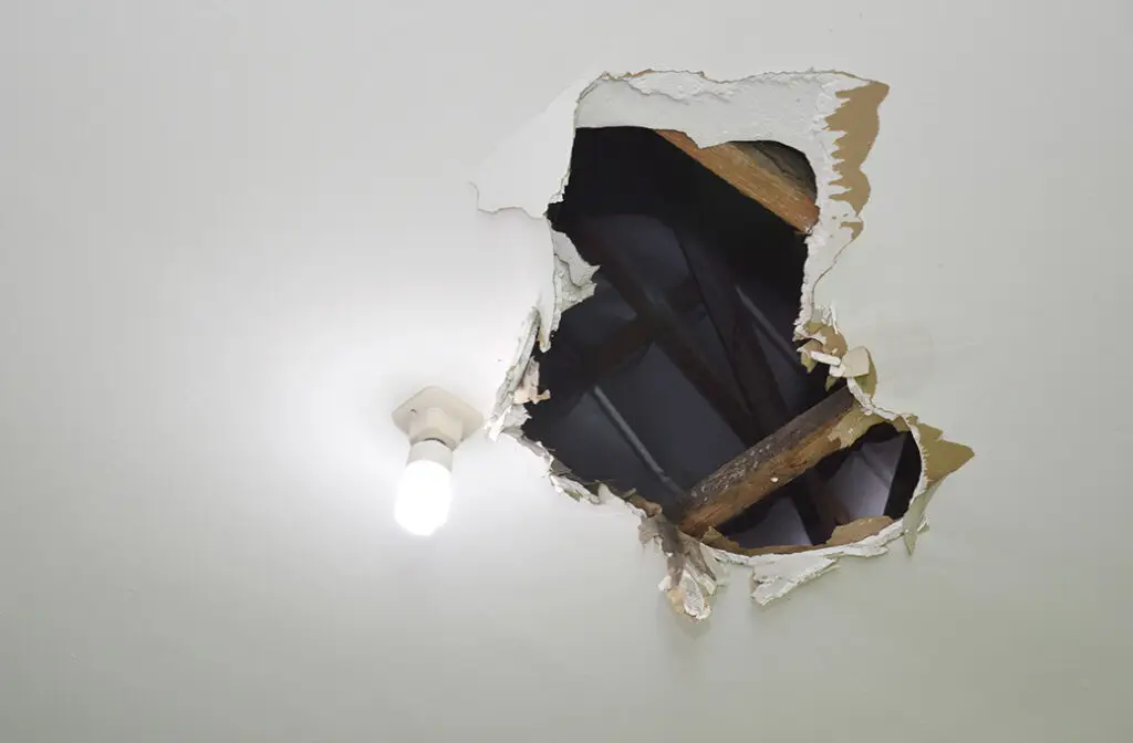 Large hole in ceiling near light fixture, exposing wooden beams