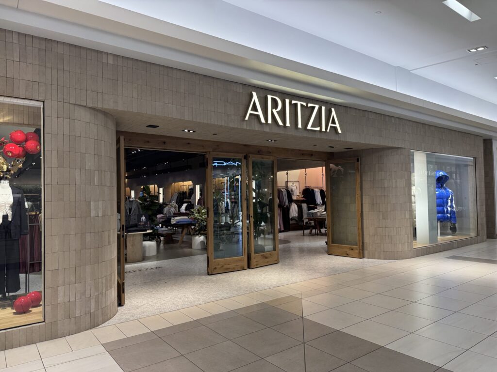 Aritzia storefront with beige brick facade and large glass doors.